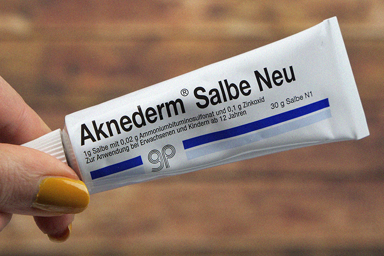 Aknederm Salbe weiße Tube vor Holzhintergrund